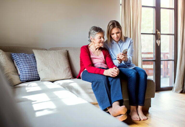 Elderly grandmother and adult granddaughter with smartphone at home