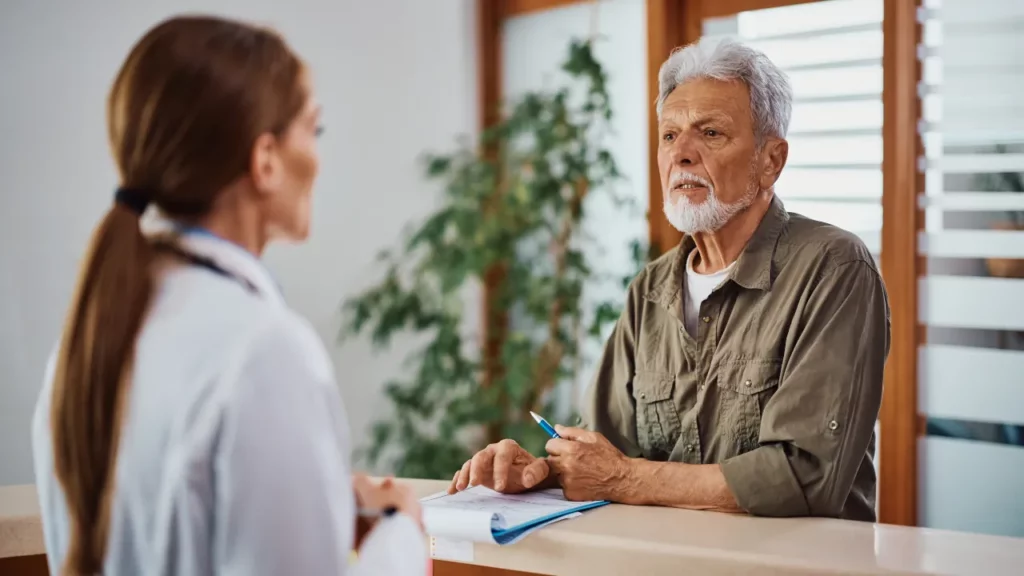 senior man communicating with healthcare provider at reception desk