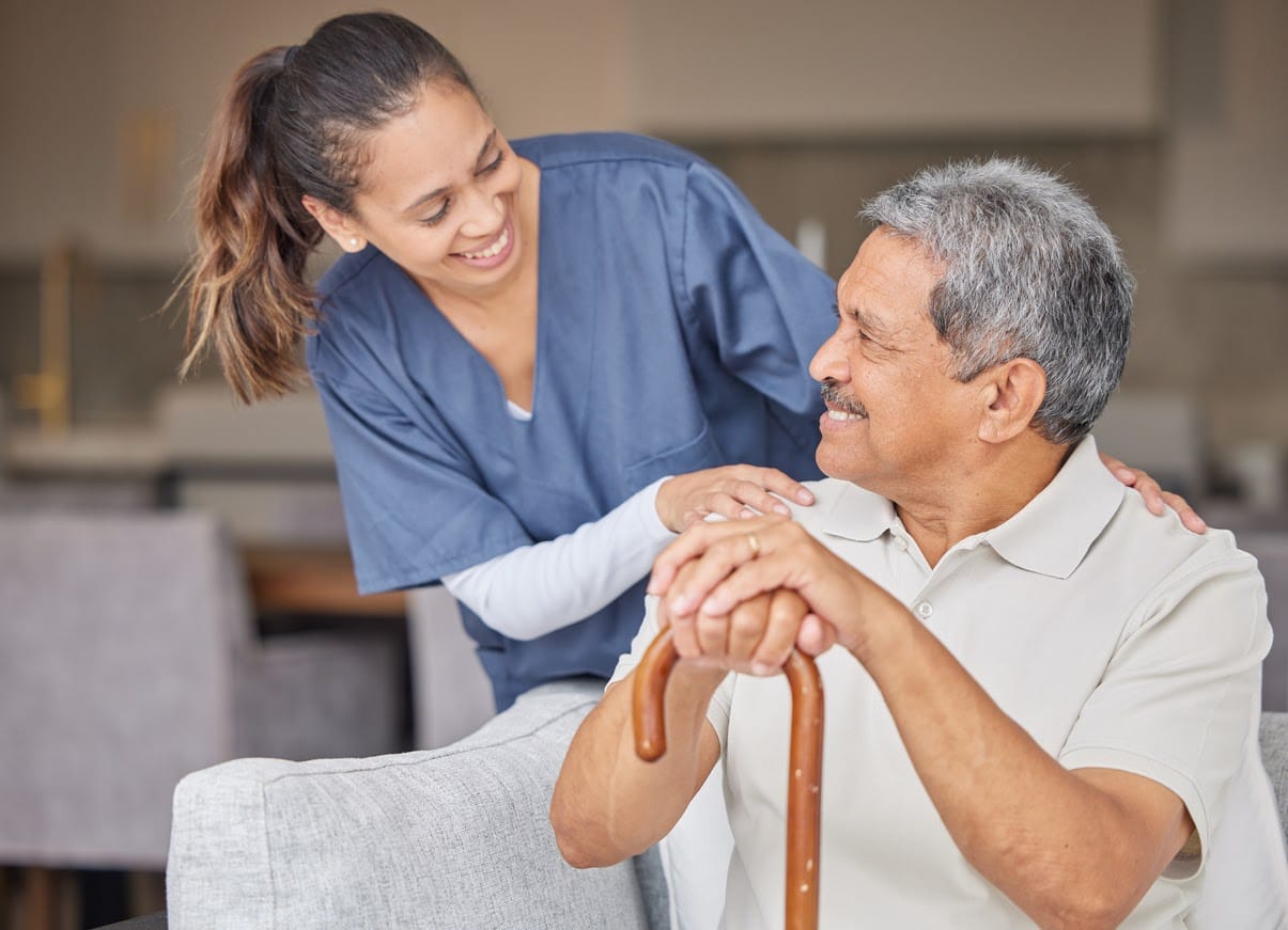 A carer sitting beside an older woman in an armchair, holding her hand A carer sitting beside an older woman in an armchair, holding her hand